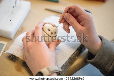 Close-up of artist's hands using a special needle to create a needle felted animal toy from wool roving, demonstrating the delicate process of needle felting