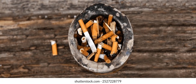 Closeup of an ashtray filled with numerous cigarette butts on a wooden surface, symbolizing smoking habits and litter, smoking harm, urban pollution, unhealthy lifestyle, littering. - Powered by Shutterstock