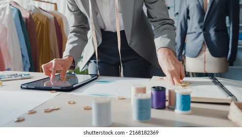 Close-up Asia Businesswoman Dressmaker With Fashion Collection Background Busy On Sketch Book Compare Draw On Digital Tablet On Table In Studio Workplace, Dress Pattern And Designer On Messy Table.