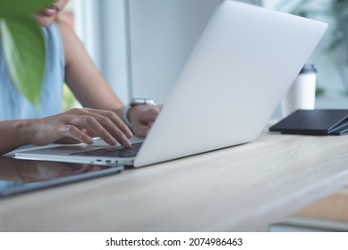 Closeup of asian business woman working on laptop computer, surfing the internet with mobile phone, digital tablet on table. Young female freelancer wearing smartwatch online working from home office - Powered by Shutterstock