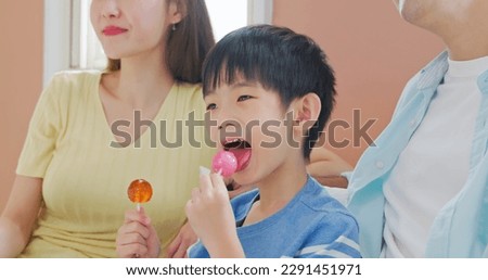 closeup asian children eat unhealthy high calories sugary food sweet candy lollipops watching TV with father and mother - parenthood ignorant careless