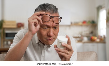 closeup of asian elderly male with presbyopia holding and looking at a pill container with confusion. He squints his eyes trying to see the instruction on bottle clearly - Shutterstock ID 2167683017