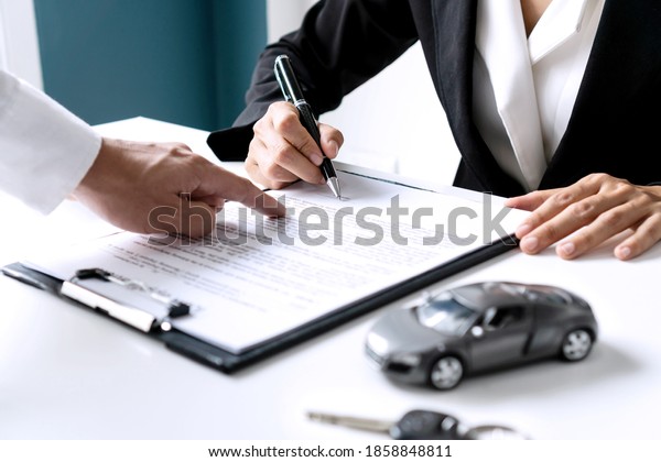 Closeup of Asian female signing car\
insurance document or lease paper contract or agreement. Buying or\
selling new or used vehicle with car keys on\
table.