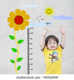 Closeup Asian Kid Stand For Measure Height With Cute Cartoon Sunflower At The Marble Stone Wall Textured Background