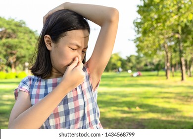 Closeup asian little girl feel bad foul odor situation,smelling,sniffing her wet armpit in outdoor park,child feeling smell of sweat, problems due to hormonal changes,motion facial expression reaction