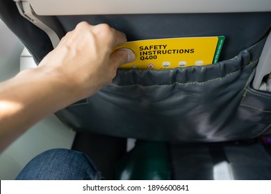 Close-up Of Asian Male's Hand Picking Aircraft Safety Card Or An Emergency Information Instruction Manual From The Airplane Seat Pocket In Front Of Him. Safety Card To Be At Every Seatback On Airplane