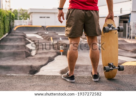 Closeup Asian man holding surfskate or skate board in pumptrack skate Park when sunrise time over photo blur of pumptrack curve, extream sport, healthy and exercise, fashion in covid19 concept