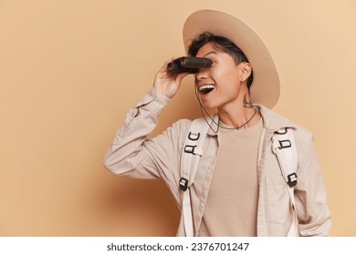 Close-up of asian man wearing big hat and backpack holding binoculars at his eyes, look around time concept, copy space - Powered by Shutterstock