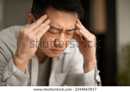 Closeup of asian middle aged man suffering from headache, touching his temples, sitting with closed eyes, copy space. Migraine, headache, stress, tension problem, hangover concept