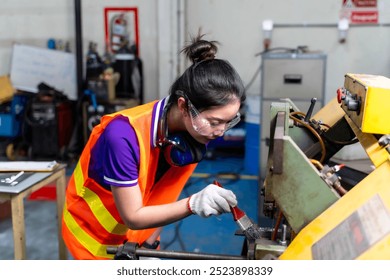 Closeup Asian woman industrial engineer in vest looking and use a cleaning brush to clean dust and scraps on the old lathe and drilling electric machine at industrial workshop. - Powered by Shutterstock