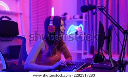 Close-up of Asian young adult woman sitting at gaming table and enjoying playing an online game. A female gamer is concentrating on playing a multiplayer game and wants to be the winner in this round.