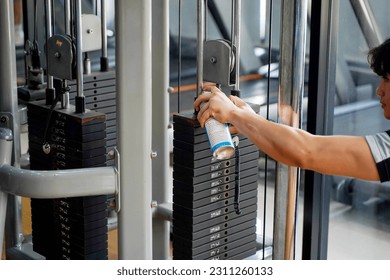 Closeup Asian young officer of fitness center spray lubricant on the weights of the weight lifting machine.