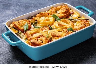 close-up of asparagus ham casserole topped with sponge cake circles in baking dish on concrete table