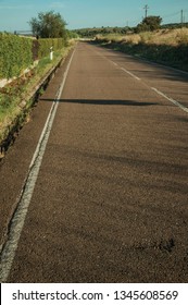 Close-up Of Asphalt On A Road Next To Grass Ditch And Green Bushes On Sunset Near Elvas. A Gracious Star-shaped Fortress City On The Easternmost Frontier Of Portugal.