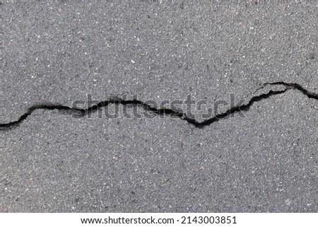 close-up asphalt road with large long crack, top view of breaking tarmac asphalt road surface, earthquake effect causes ground to damaged, abstract texture background