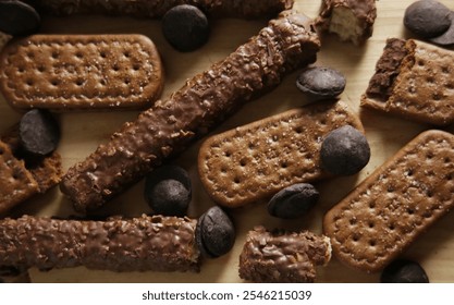 Close-up of assorted chocolate-coated wafers and rectangular biscuits arranged on a wooden board with chocolate buttons scattered around. Flat lay.  - Powered by Shutterstock