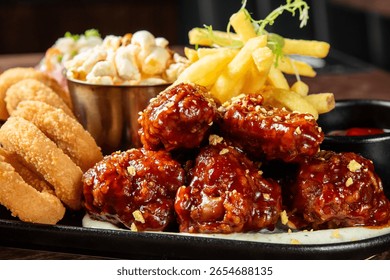 Close-up of assorted fried snacks including crispy onion rings, saucy chicken wings, French fries, and popcorn on a plate. Tasty fast food with rich texture and color.
