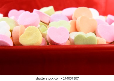 Closeup Of Assorted Pastel Candy Hearts For Valentines Day In A Red Ceramic Candy Bowl. Shallow Depth Of Field. The Candies Are Blank And Ready For You To Add Your Own Message.