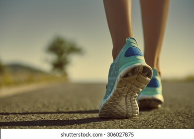 Closeup of athlete female feet in running shoes jogging on the road early in the morning. Healthy lifestyle.
