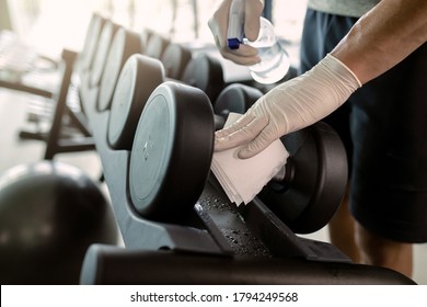 Close-up Of Athlete Wearing Protective Gloves And Disinfecting Hand Weights At Health Club. 