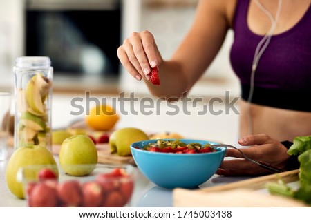 Close-up of athletic woman eating healthy and preparing fruit salad in the kitchen. 