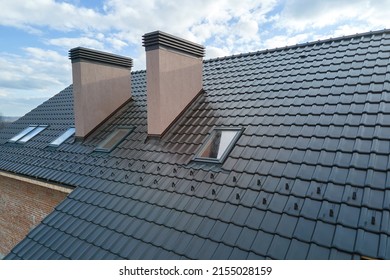 Closeup of attic windows and brick chimneys on house roof top covered with ceramic shingles. Tiled covering of building