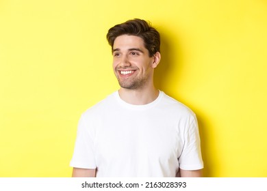Close-up of attractive bearded man in white t-shirt smiling, looking left at copy space, standing against yellow background - Shutterstock ID 2163028393