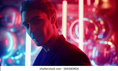 Closeup attractive man sending air kiss in nightclub. Portrait of affectionate person flirting on neon lights background. Fancy man biting lip at party.