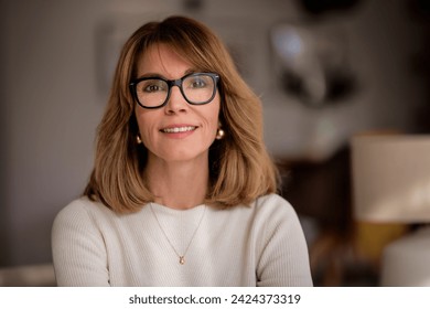 Close-up of an attractive mid aged woman relaxing in an armchair at home. Blond haired female wearing eyeglasses and white sweater and pants. - Powered by Shutterstock