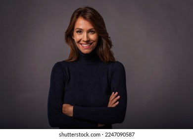 Close-up of an attractive middle aged woman with toothy smile wearing black turtleneck sweater while staning at isolated dark background. Copy space. Studio shot. - Shutterstock ID 2247090587