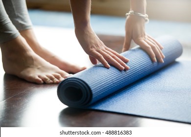 Close-up of attractive young woman folding blue yoga or fitness mat after working out at home in living room. Healthy life, keep fit concepts. Horizontal shot - Powered by Shutterstock