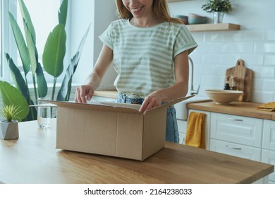 Close-up Of Attractive Young Woman Unpacking Box While Standing At The Domestic Kitchen