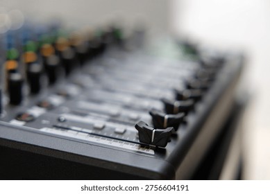 Close-up of audio mixer with knobs and sliders in focus. Blurred background emphasizes mixing equipment detail. Professional studio or live performance setup. Ideal for music production, sound design