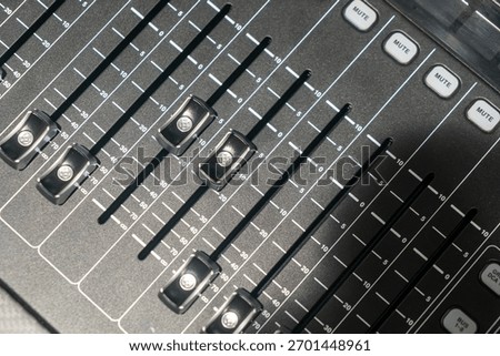 Close-up of an audio mixing console featuring multiple sliding faders, mute buttons, and volume controls, ideal for professional sound production and engineering.