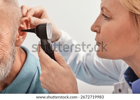 Close-up of audiologist checking elderly man ear with an otoscope during a hearing test in an audiology clinic