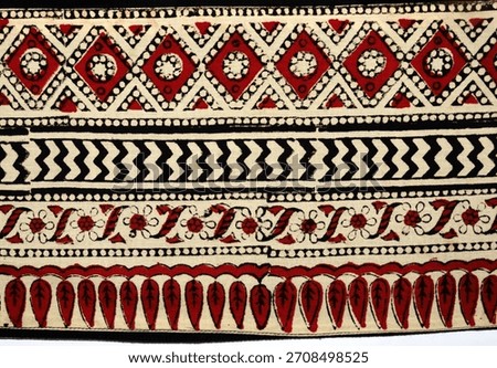 Close-up of authentic Indian hand block-printed cotton textile featuring rich red, black, and cream geometric and floral borders. Classic Ajrakh-style patterns with diamond, zigzag, and paisley