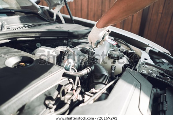 Close-up. The auto mechanic is fixing a\
car with a wrench. White car. White gloves for\
repair