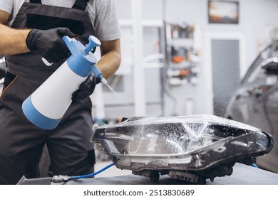 Close-up Auto technician cleaning car headlight with spray bottle in repair garage. Focus on cleanliness and detailing using protective gloves for safety and precision. - Powered by Shutterstock