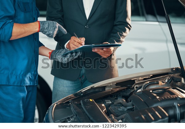 Close-up of\
auto technician in gloves pointing his client where he should to\
sign before repairing his car in\
workshop