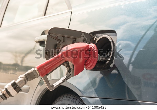 Close-up a automatic fuel nozzles filling into\
car tank. Gas pump nozzle in fuel tank of blue car at gas station\
in Texas, America. Auto shut-off gas nozzle refilling. Fuel,\
energy, ecology\
concept.