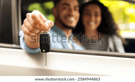 Closeup of automatic key from car in middle-eastern guy driver hand, blurred background. Unrecognizable arabic couple sitting inside nice automobile, showing key from auto, car renting concept