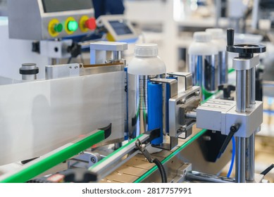 Close-up of an automatic labeling machine applying white paper labels to plastic bottles moving along a conveyor belt in a modern manufacturing plant.
