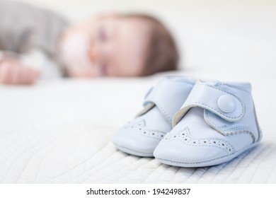 Closeup Of Baby Blue Leather Shoes Over A Bed And Adorable Babe Sleeping On The Background