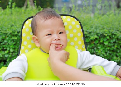 Close-up Baby Boy Sitting On Kid Chair Eating With Something Stuck In His Mouth And Mother Help To Keep Out.