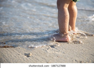 close-up baby feet in the sand and waves of the sea