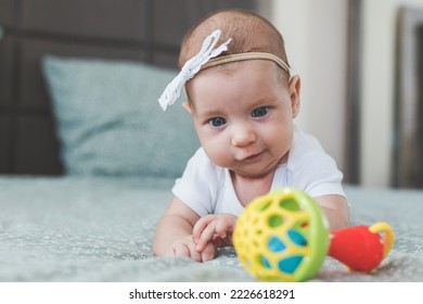 close-up of a baby girl 2 months old, lies on her stomach with a rattle, looks at the toy, the concept of newborn, infancy - Shutterstock ID 2226618291