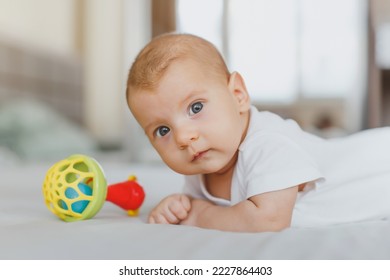 close-up of a baby girl 2 months old, lies on her stomach with a rattle, looks at the camera, the concept of newborn, infancy - Shutterstock ID 2227864403