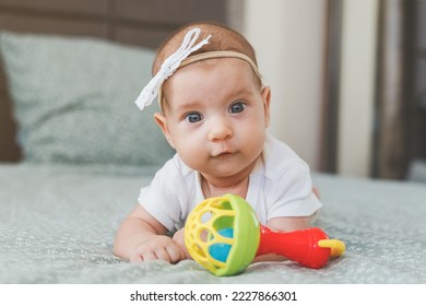 close-up of a baby girl 2 months old, lies on her stomach with a rattle, looks at the camera, the concept of newborn, infancy - Shutterstock ID 2227866301