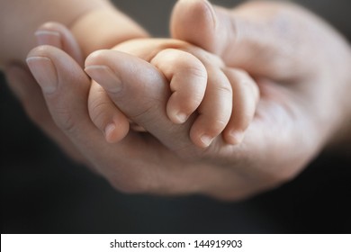 Closeup of a baby holding man's finger against black background