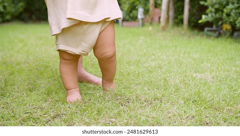 Close-Up of Baby's Legs Taking First Steps on Green Grass in Garden, Outdoor Toddler Exploration, Childhood Milestone, Natural Environment, Early Development, Innocence and Growth - Powered by Shutterstock